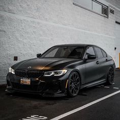 a black bmw is parked in front of a white brick building with yellow doors and windows