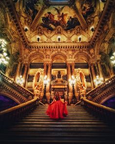 two women in red dresses are walking up the stairs to an ornate building with chandeliers