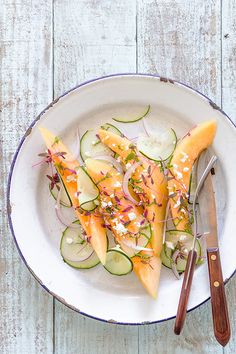 a white plate topped with sliced cucumbers and other veggies next to a knife