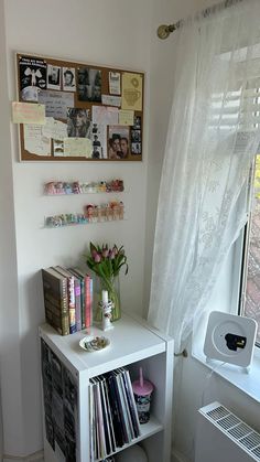 a small white shelf with books and magazines on it in front of a window filled with pictures