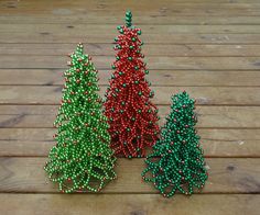 three small christmas trees made out of beads on a wooden floor, one red and one green