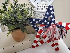 a red, white and blue star decoration next to a potted plant with a clock in the background