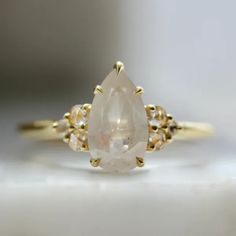 a yellow gold ring with a pear shaped white diamond in the center and three small diamonds around it