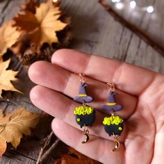 a hand holding two small earrings in the shape of witch's hat and broom