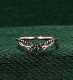 a gold ring with black stones on it sitting on a green surface in front of a dark background