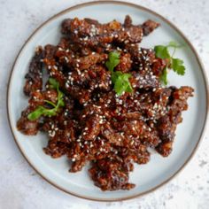 a white plate topped with meat covered in sesame seeds and garnished with cilantro