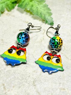 two colorful earrings with black and white dots on them sitting next to a green leaf