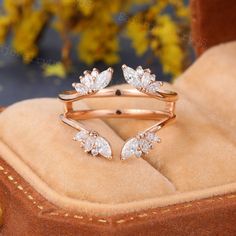 two gold rings with white stones on them sitting on a velvet cushion in front of flowers