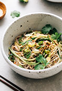 a white bowl filled with noodles and vegetables next to chopsticks on a table