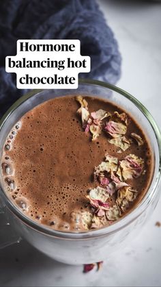 a glass mug filled with chocolate and flowers on top of a white table next to a blue blanket