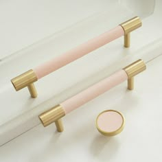 two pink and gold handles on a white wall next to a small round object in the middle