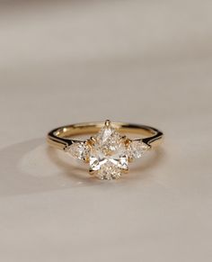 a yellow gold ring with three pear shaped diamonds on the band and an oval cut diamond in the center