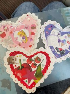 three heart shaped stickers sitting on top of a table next to a person's legs