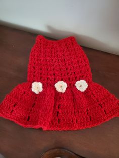 a crocheted red dress with white flowers on the front and bottom, sitting on a table