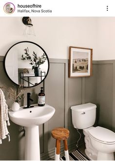 a white toilet sitting next to a bathroom sink under a round mirror on a wall