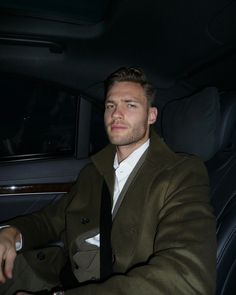 a man sitting in the back seat of a car wearing a brown suit and white shirt