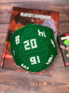 a green knitted dice sitting on top of a wooden table next to a book