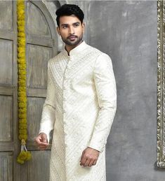 a man standing in front of a wooden door wearing a white sherwanit