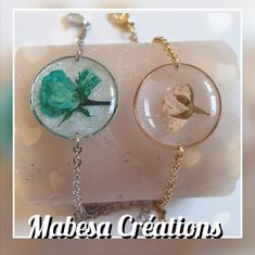 two necklaces that have flowers in them on some kind of rock with chains attached to it