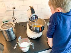 a young boy standing in front of a kitchen counter with an electric mixer on it