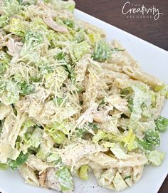 a white plate topped with pasta and lettuce covered in cheese dressing next to a fork