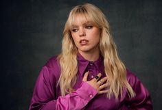 a woman with blonde hair wearing a purple shirt and black ring on her left hand