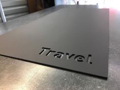 the word travel is engraved on an aluminum surface in front of a metal table top