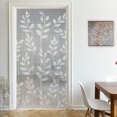 a dining room table and chairs in front of a window with white leaves on it