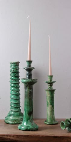 three green candlesticks sitting on top of a wooden table next to each other