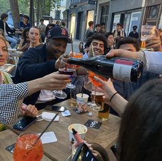 a group of people sitting at a table with drinks and wine glasses in their hands