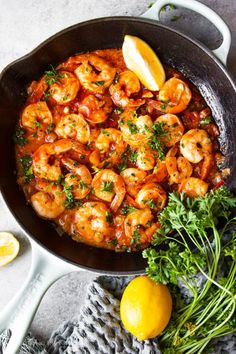 a skillet filled with shrimp and lemons on top of a table next to some parsley