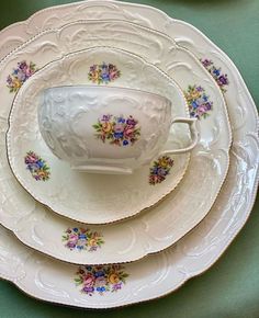 a stack of white plates with floral designs on them, sitting on a green table cloth