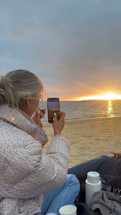 a woman sitting on the beach taking a photo with her cell phone