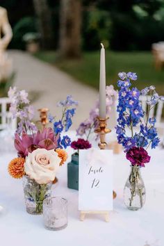 flowers in vases on top of a table with a sign and candlestick next to it