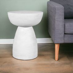 a white vase sitting on top of a wooden floor next to a gray couch and chair