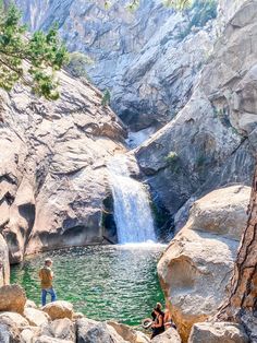 two people sitting on rocks in front of a waterfall with water coming out of it