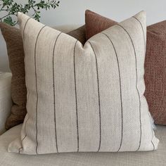 three pillows sitting on top of a couch next to a potted plant in a vase