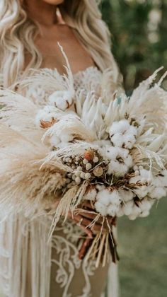 a woman in a white dress holding a bouquet filled with flowers and feathers on her wedding day