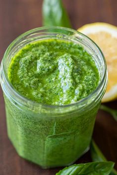 a glass jar filled with green pesto next to an orange and some basil leaves