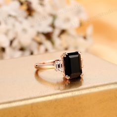 a black diamond ring sitting on top of a gold box with flowers in the background