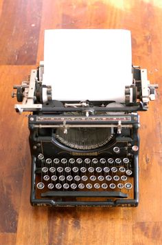 an old fashioned typewriter sitting on top of a wooden table next to a white piece of paper