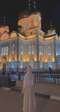 a woman standing in front of a large building with lights on it's sides