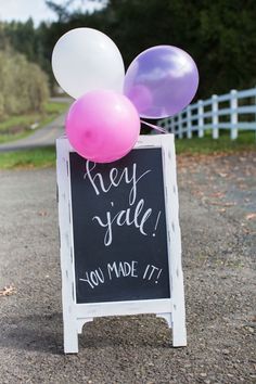 a chalkboard sign with balloons attached to it that says hey y'all you made it