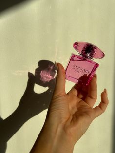 a woman's hand holding a pink perfume bottle in front of a white wall