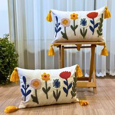 two decorative pillows with tassels and flowers on them sitting on a wooden chair