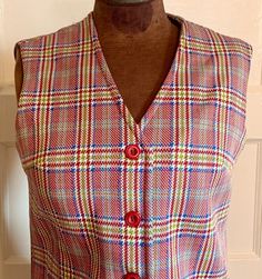 "Definitely 100% polyester. Seems to be in good shape, with no visible tears snags, or stains.  It is a sleeveless button up vest with a plaid pattern on white. Colors are red, blue, and green.  There is no maker's tag. It has pockets. Seems to be a medium to large.  Measurements when laid flat are approximately: Shoulder to shoulder 15\" Armpit to armpit 19.5\" Bust 18.5\" Waist 18\" Shoulder to hem 26.5\" Bust circumference 37\" max  Waist circumference 36\" max Arm hole opening circumference Retro Red Sleeveless Vest, Red Sleeveless Retro Vest, Red Cotton Retro Vest, Retro Red Cotton Vest, Vintage Red Vest Top, Red Retro Cotton Vest, Red Sleeveless Vest With Buttons, Vintage Red Vest For Summer, Red Vintage Vest For Summer