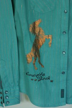 wrangler cowgirl shirt. size S but it fit's more like an XS. teal cotton with a gold metallic thread. snap closure down the front and at the cuffs. gold transfers of a horse and guitar's. star and circle rivet embellishments. 'cowgirls rock' embroidered on the lower right side. western cut at the yoke front and back. very good vintage condition, no stains, holes or flaws. by wrangler. shoulder width  15bust at armpit 36sleeve  24length  23.25 Western Style Cotton Shirt For Spring, Trendy Fitted Tops For Rodeo, Long Sleeve Tops For Summer Rodeo, Western Style Relaxed Fit Shirt For Spring, Summer Long Sleeve Tops For Rodeo, Fitted Cotton Western Top, Fitted Cotton Top For Rodeo, Fitted Gold Cotton Top, Fitted Western Style Cotton Shirt