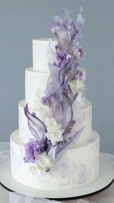 a three tiered white cake with purple and white flowers