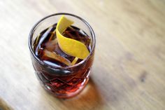 a close up of a drink with an orange peel on the top and some ice