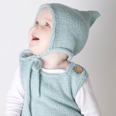 a young child wearing a knitted hat and vest with buttons on the hood, looking up